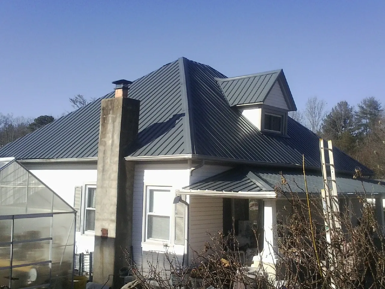 Dark blue standing seam metal roof on a white farmhouse with dormer — Slate & Tile Roof Repair by Roofing Brothers in Angola
