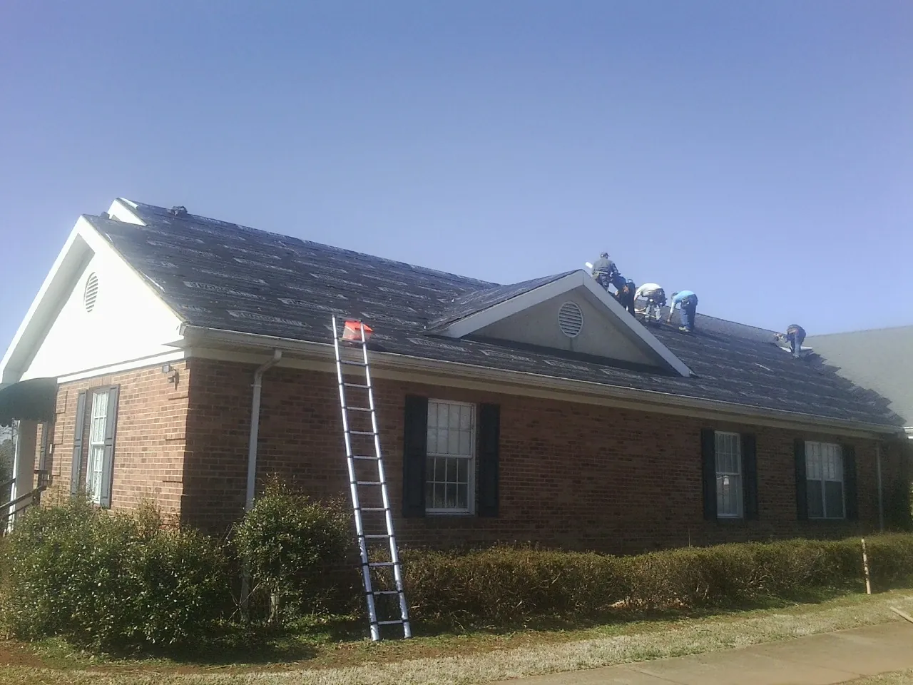 Crew tearing shingles off a brick ranch roof with a ladder set — Emergency Roof Repair work by our crew in Angola